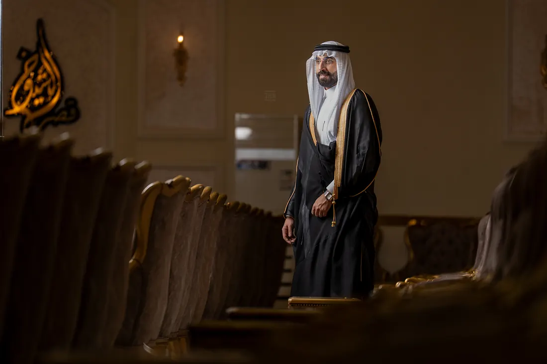 عريس يقف وحيدًا عند طرف قاعة الاحتفال خلف صف من الكنب المذهّب