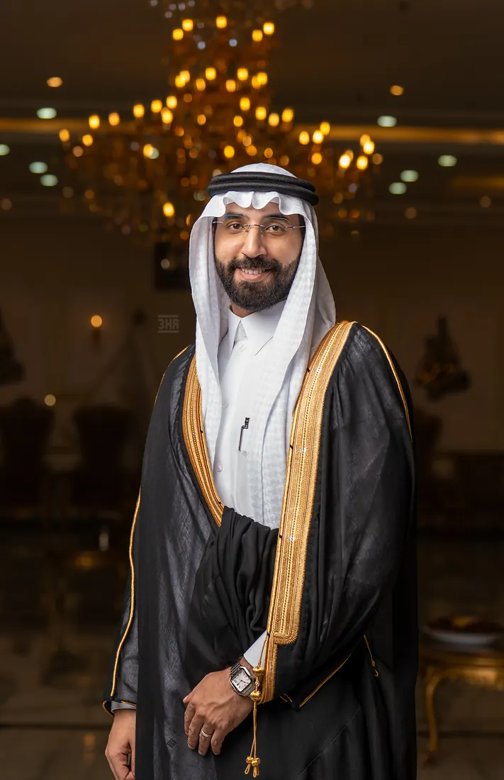 العريس واقفًا بالبشت تحت الثريا مبتسمًا